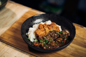 Japanese chicken katsu curry rice, deep fried breast chicken fillet with beef, carrot and potato curry in black plate on wooden table Crispy fried pork cutlet with curry rice  - Japanese food style