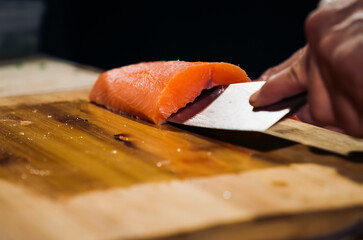Close up of Chef cook hands chopping salmon fish for traditional Asian cuisine with Japanese knife....