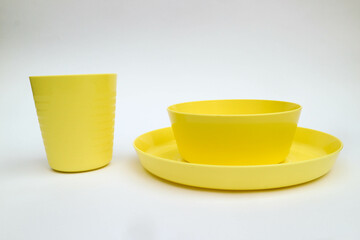 Yellow plastic dinnerware, bowl, plate and cup isolated on white background