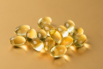Vitamin E. Supplementary food. Omega 3. Gold fish oil gel Capsules on gold background.