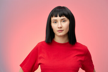 Fototapeta premium horizontal photo of a cute, beautiful woman with short black hair looking pleasantly into the camera standing on a gray background with red lighting in a red T-shirt