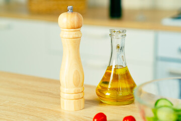Pepper mill, olive oil in jug for adding to food on table in kitchen.