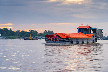 A large covered barge cruising down a river at dawn in Chau Doc, Vietnam