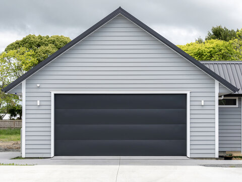 Typical double detached gray garage with black tilt-up retractable raised panel metal door and gable metal roof