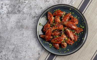 Honey Glazed Chicken Wings with sesame seeds and herbs on a round plate on a dark gray background. Top view, flat lay