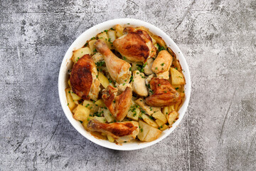 Homemade Roasted Chicken with Potatoes, onions and herbs  in a white baking dish on a dark grey background. Top view, flat lay