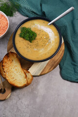 red lentils soup puree in dark bowl with bread on grey marble table