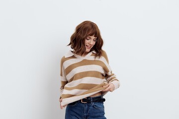 a sweet, beautiful, pretty woman stands on a white background in a striped long sweater and corrects it. Fashion-themed photography