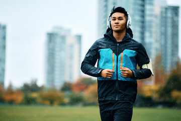 Young sportsman listens music on headphones while running in rain.