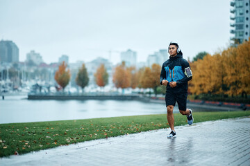 Young sportsman jogging at riverbank on rainy day.