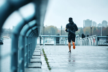 Back view of male athlete running on street during rainy day.