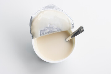 Top view of a cup of plain non-dairy full-fat yogurt alternative made from oat milk isolated on a white background. Opened cup with a spoon in it. Ready to enjoy.