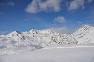 Aerial of snowy mountain slopes full of powder for freeride at ski resort on winter sunrise. Mountains range of backcountry covered with virgin snow. Caucasus peaks skyline with twilight afterglow.