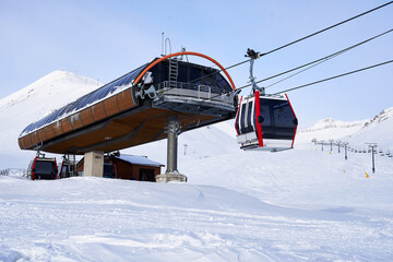 Cable car gondola at ski resort with snowy mountains on background. Modern ski lift with funitels and supporting towers high in the mountains on winter day. Ski lift station with no people.