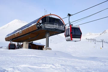 Photo sur Aluminium Gondoles Cable car gondola at ski resort with snowy mountains on background. Modern ski lift with funitels and supporting towers high in the mountains on winter day. Ski lift station with no people.