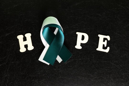 Top view of with word hope teal and white ribbon in dark black background. Cervical cancer hope and awareness concept.