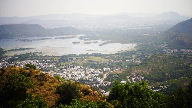 panning video shot showing an aerial drone view of Udaipur rajasthan the city of lakes with green tree covered aravalli hills and densely packed houses from Sajjan garh monsoon palace