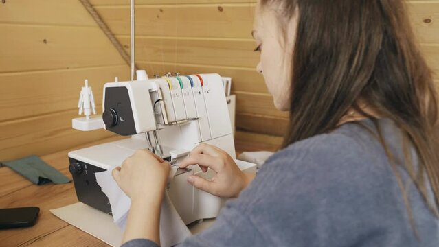 A woman designer works on an overlock sewing machine on tailoring. Small tailoring business.