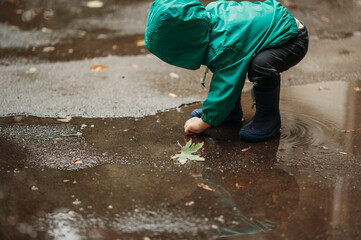 Happy boy playing outside on a rainy day wearing rubber boots and jacket