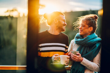 Young couple drinking coffee or tea while standing on their balcony at sunrise