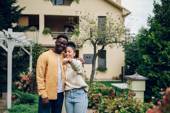 Multiracial couple holding keys and standing outside their new home