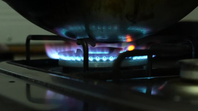 A blue fire and flame are pent up and glowing from gas stove in the low light environment for warming the steel pan for cooking food in family house.