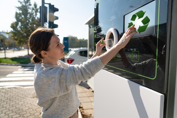Woman uses a self service machine to receive used plastic bottles and cans on a city street	