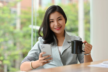 Portrait of Millennial Smart Businesswoman holding mobile  phone and a cup of coffee.