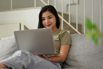 Fototapeta premium Millennial Asian woman using laptop while sitting on sofa, Shopping online, Chatting in social network, Watching movie or Working.