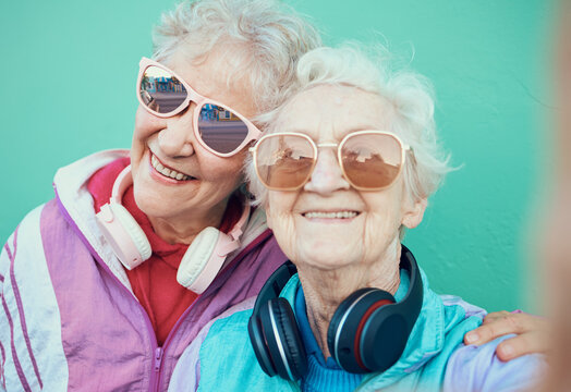 Senior women, fashion and retro selfie friends with sunglasses, headphones and vintage clothes in retirement. Portrait of cool old people together for pop art and hug profile picture against wall