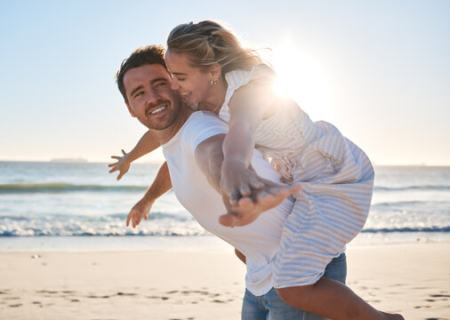 Happy, Couple And Piggyback Walk On The Beach For Love, Travel Or Summer Vacation Bonding Together In The Outdoors. Man Carrying Woman On Back With Smile Enjoying Playful Fun Time Walking By The Sea