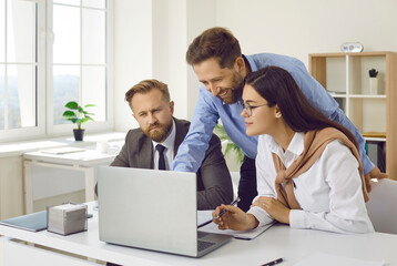 Team of confident business people analyzing data using laptop computer. Male and female employees looking at laptop together in office interior. Successful colleagues brainstorming, discussing ideas