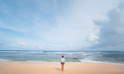 Vacation on the shore. Young woman standing on tropical beach enjoying beautiful view. © Loginova