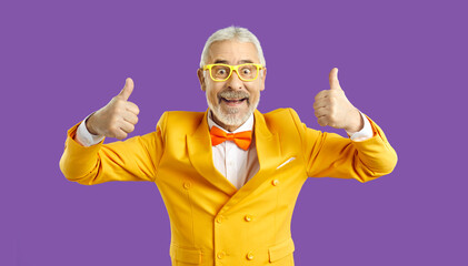 Cheerful funny charismatic senior man showing thumbs up isolated on purple background. Mature man...