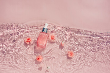 Transparent pink bottle of serum in water with flowers, texture of ripples waves