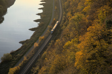 A train travels on a curved railway track through a rural landscape of trees, forest, mountains and...