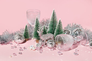 Christmas and New Year table creative layout with christmas decoration, wine glasses and christmas trees on pastel pink background. Winter idea. 80s or 90s retro aesthetic party celebration concept.