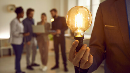 Man in suit holding bright electric Edison light bulb as symbol of developing creative business...
