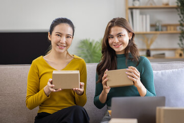 Two Asian women to Startup small business SME entrepreneur of freelance working on laptop computer with parcel box on table laptop at home, online marketing packaging and delivery SME idea concept