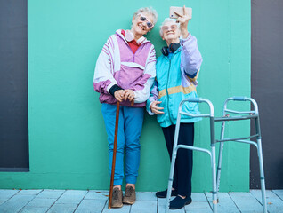 Phone, selfie and disability with senior friends posing for a photograph outdoor on a green wall background. Happy, mobile and walker with a mature woman and friend taking a picture together