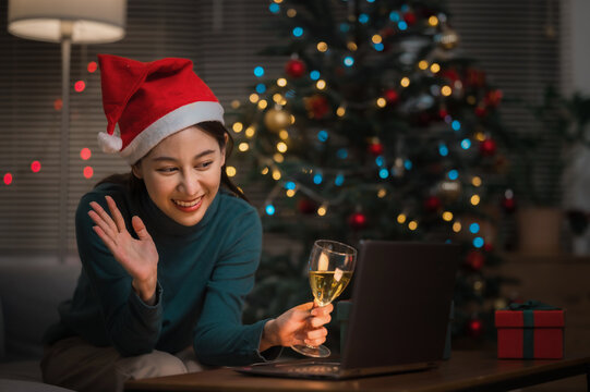 Asian woman wearing Christmas hat drinking champagne video call celebrate Happy New Year party online with her friends or family via laptop at home