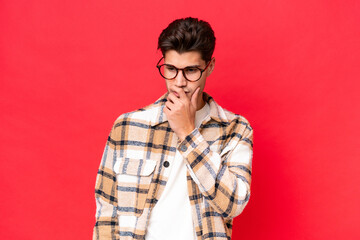 Young caucasian handsome man isolated on red background having doubts