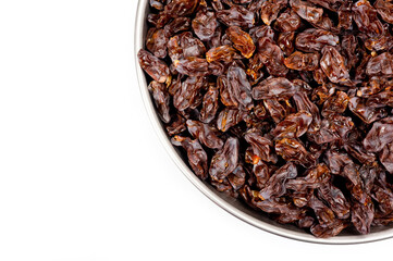 Dark-colored raisins lying in a metal container, shot on a white background.