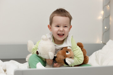 happy cheerful child 3 sits in bed and laughs, hugs toys, wake up in the morning