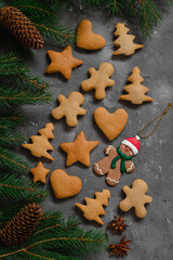 Christmas composition with fresh gingerbread cookies, gingerbread man Christmas toy fir tree branches, cones, star anise on a grey background.