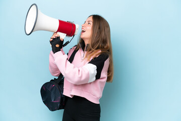 Young sport woman with sport bag isolated on blue background shouting through a megaphone