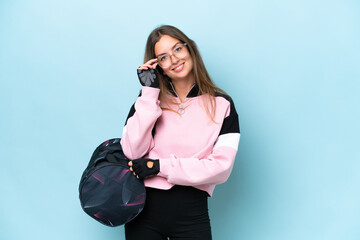 Young sport woman with sport bag isolated on blue background with glasses and happy