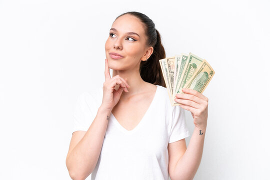 Young caucasian woman taking a lot of money isolated on white background thinking an idea while looking up