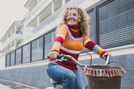 Happy middle age active woman riding a bike in the city wearing colorful sweater. Green transport mode and outdoor urban leisure activity with pretty female people using bike. Healthy lifestyle lady