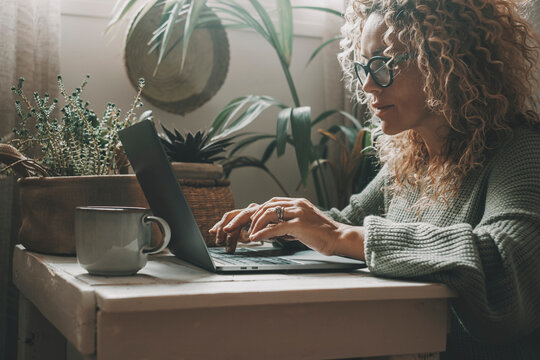 One Woman At Home Using Laptop In Green Mood Color Background And Ambient. House Indoor Garden In Background. Attractive Female People Use Computer For Work Or Surf The Web In Indoor Leisure Lifestyle